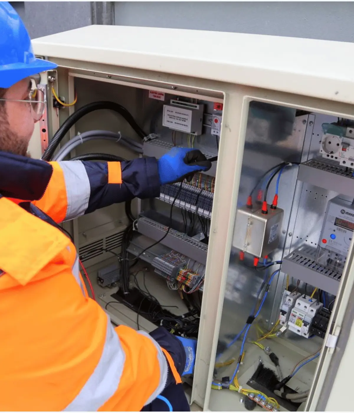 Électricien casqué intervenant sur les borniers d'un coffret électrique ouvert.