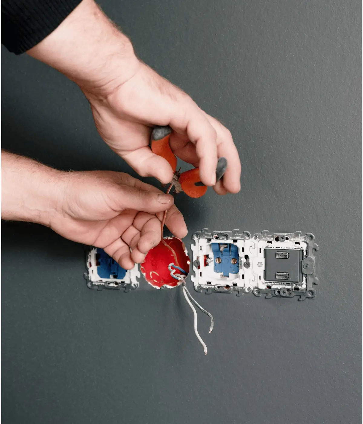 Mains d'un électricien dénudant un fil pour poser une prise et un interrupteur muraux.