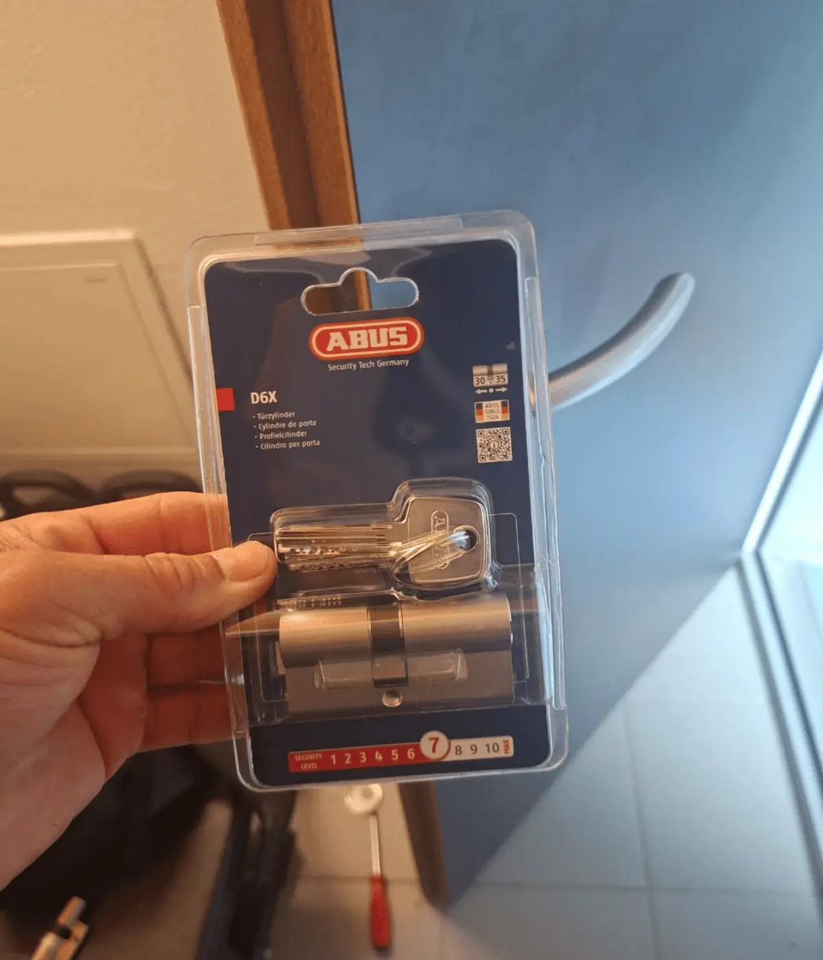 Cylindre de porte neuf, encore sous blister, présenté devant la porte à équiper.