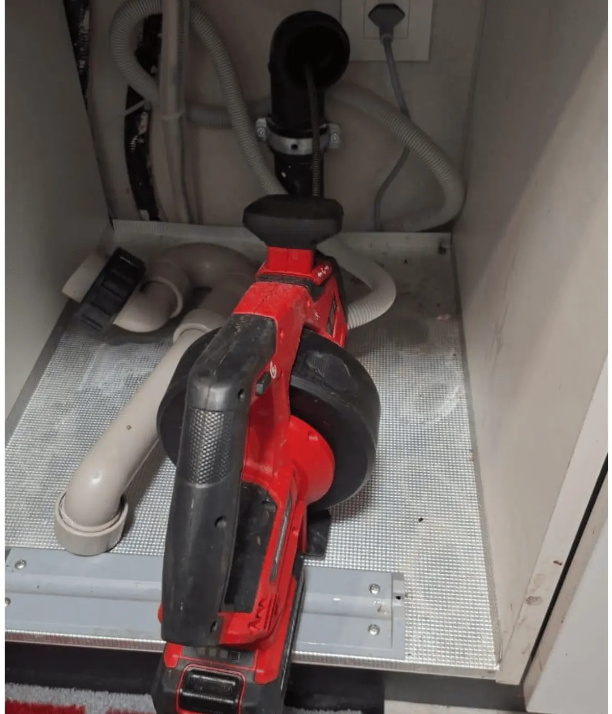 Déboucheur électrique à furet posé sous un évier, devant le siphon à dégager.