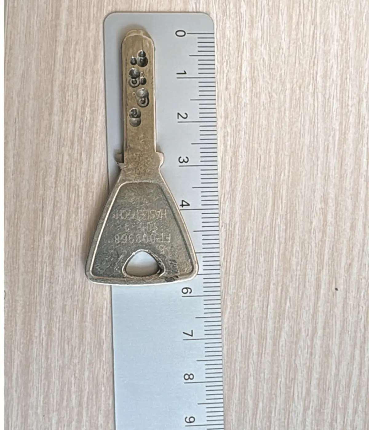 Clé de sécurité à picots mesurée sur une réglette pour identifier le cylindre correspondant.